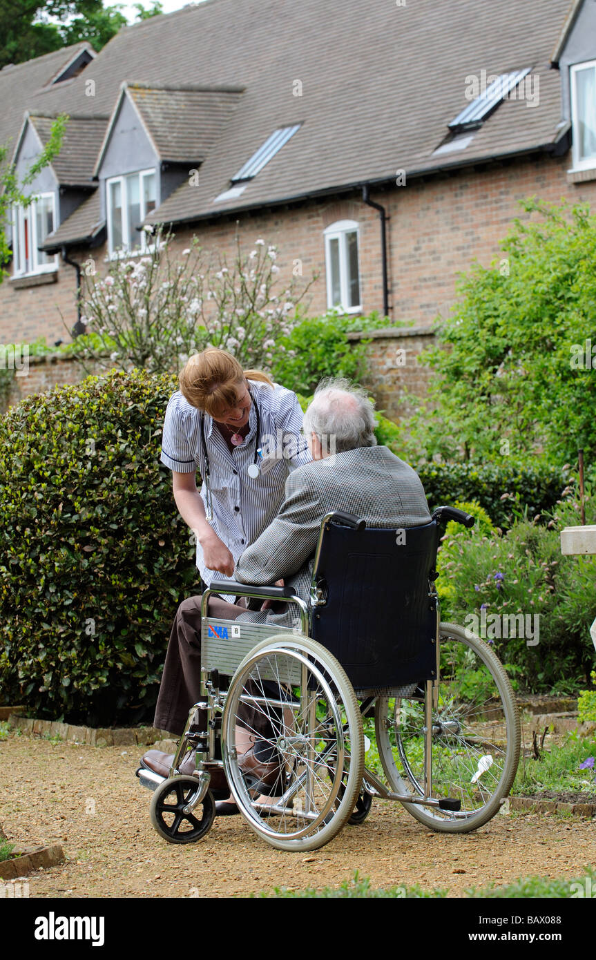 Krankenschwester, die Fürsorge für einen männlichen Patienten sitzen im Rollstuhl in einem Carehome Garten Stockfoto