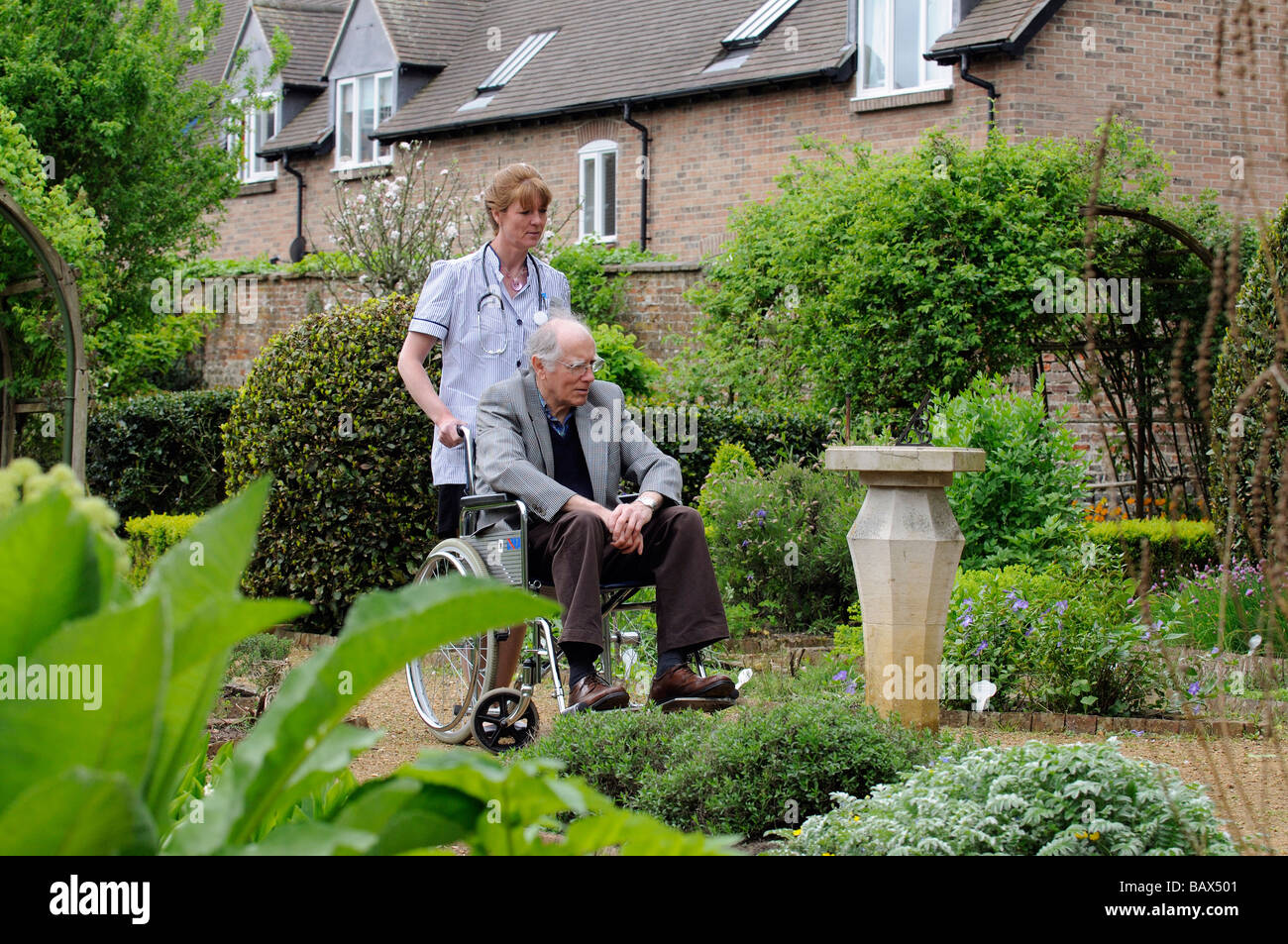 Krankenschwester schob einen männlichen Patient im Rollstuhl durch einen schönen Garten Stockfoto