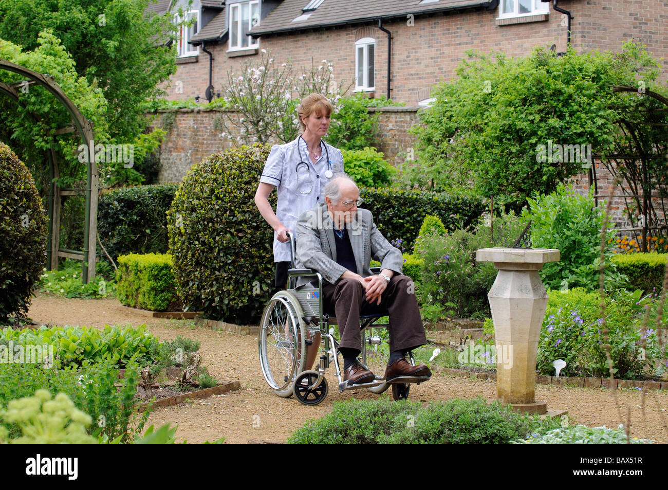 Krankenschwester schob einen männlichen Patient im Rollstuhl durch einen schönen Garten Stockfoto