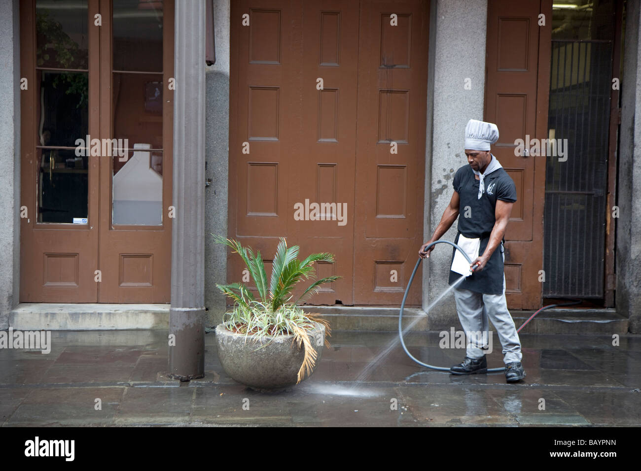 New Orleans Louisiana A Mann einen Koch s Hut reinigt den Bürgersteig vor einem Restaurant im French Quarter Stockfoto