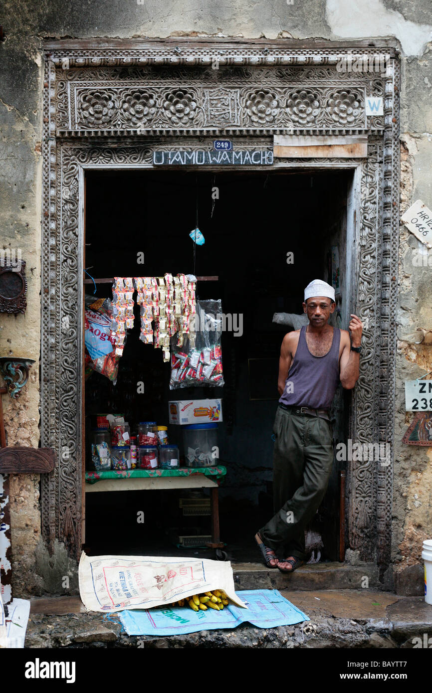 Ladenbesitzer in einem Hauseingang in Sansibar Stone Town, mit den kunstvollen traditionellen Holzschnitzerei sichtbar in der Holztür Stockfoto