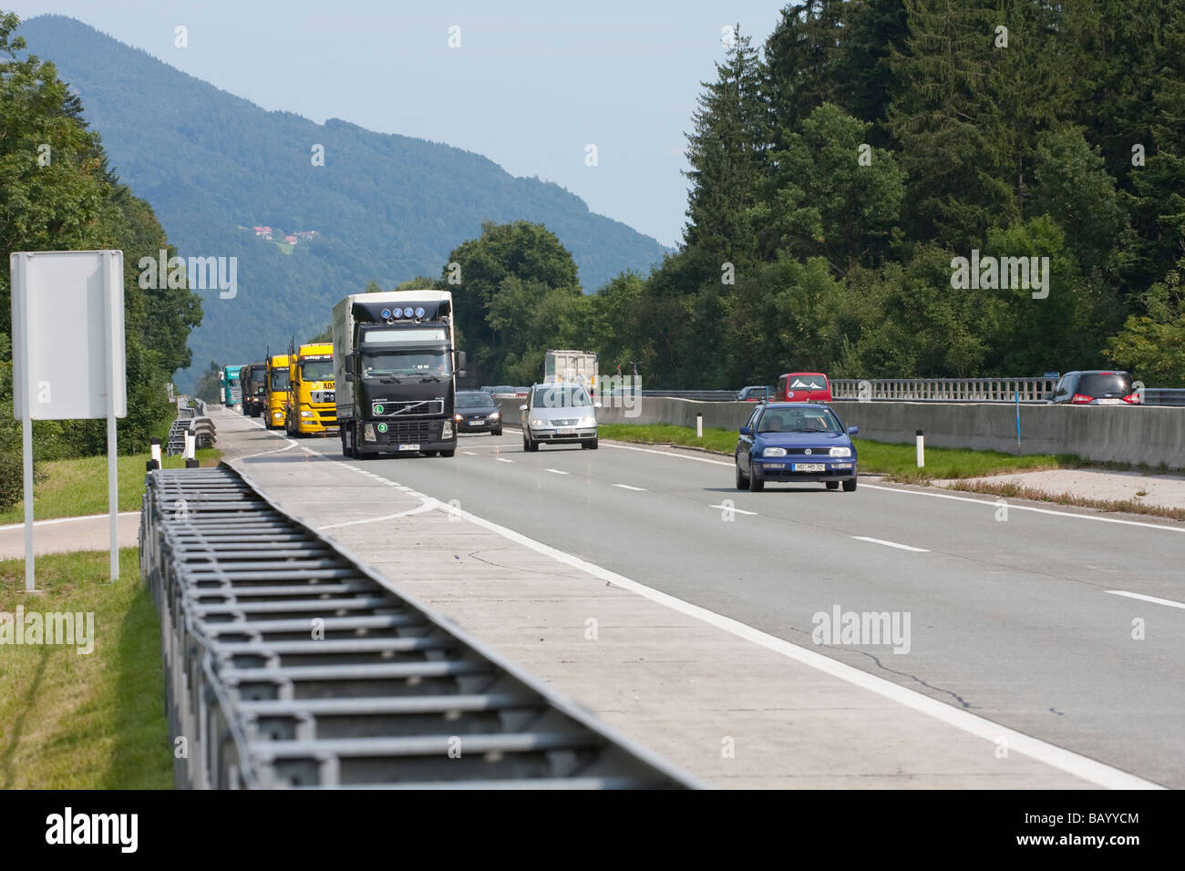 Autobahn in Österreich bei Salzburg. A1 Autobahn in Österreich an einem belebten Sommernachmittag. Zahlreiche LKWs und Autos sind vorbeifahrende zu sehen. Stockfoto