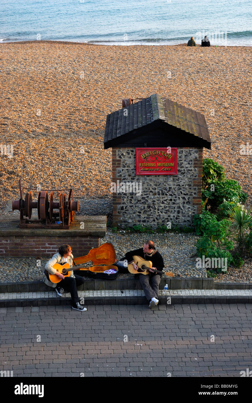 Straßenmusiker spielen Sie Musik auf Brighton Seafront zwei Leute sitzen am Strand West Sussex England UK Stockfoto