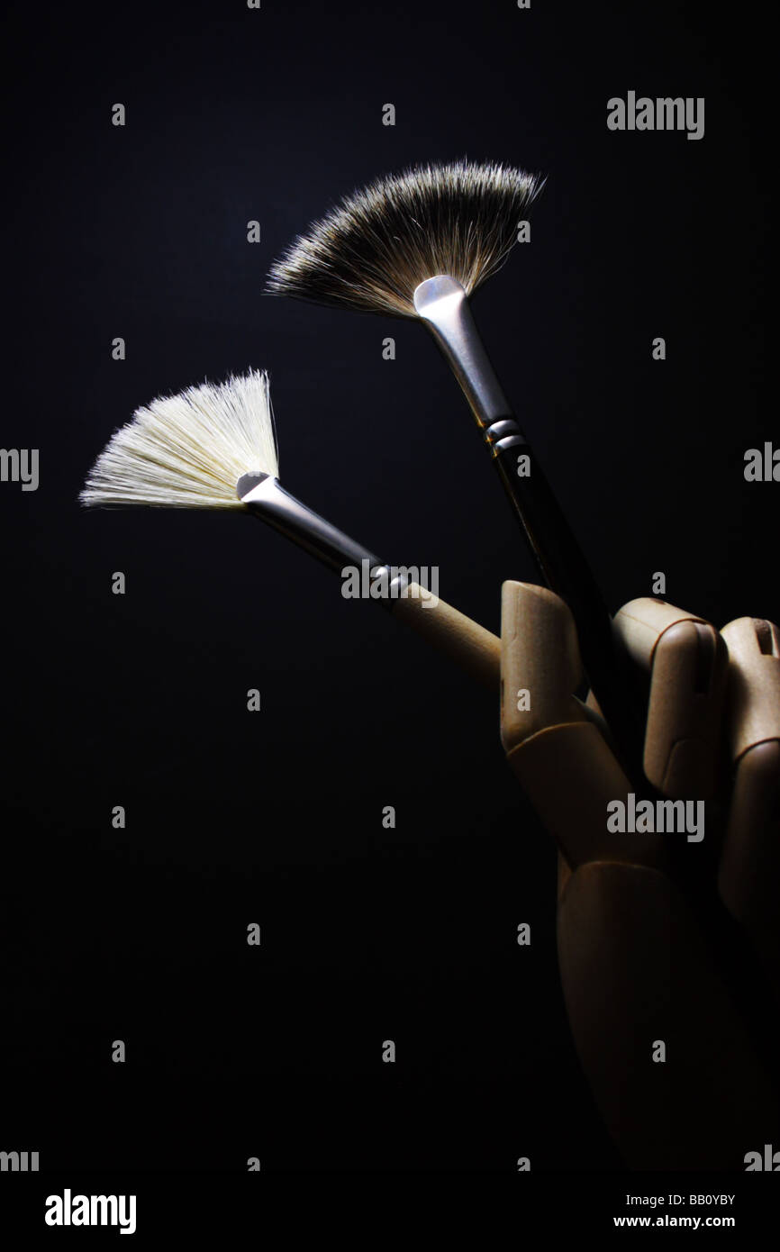 Hölzerne Hand hält zwei Pinsel vor schwarzem Hintergrund Stockfoto