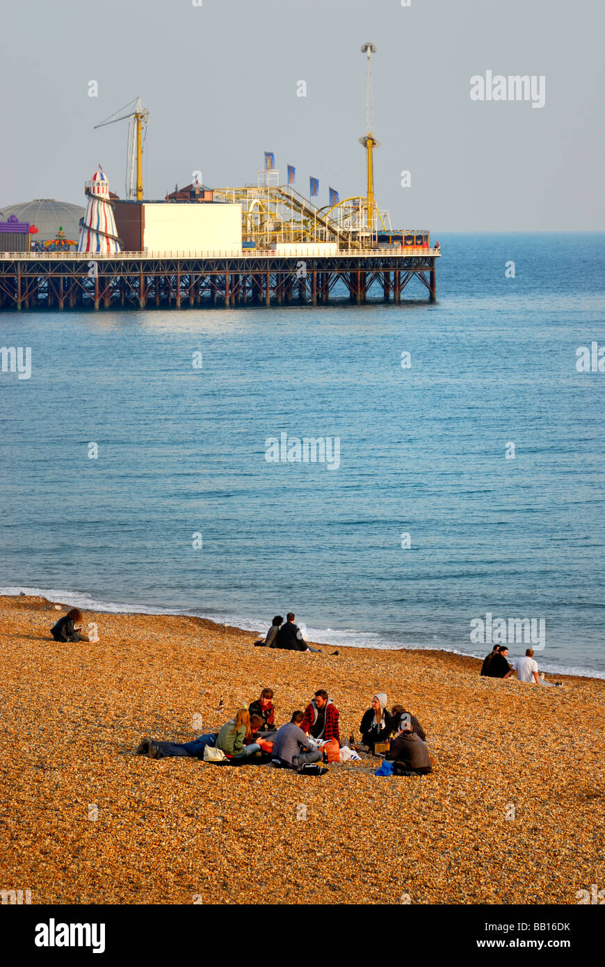 Touristen sitzen am Strand von Brighton Brighton Pier im Hintergrund Stockfoto