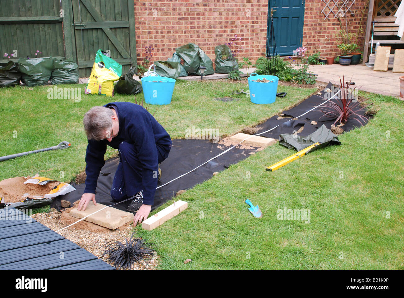 Mann, die Verlegung von Pflaster Platte in neuen Gartenweg in modernen britischen Haus Stockfoto