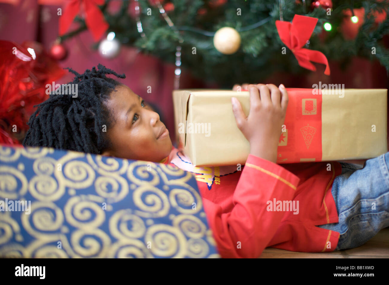 Junge Verlegung vor Weihnachtsbaum mit Gegenwart, Pietermaritzburg, Provinz KwaZulu-Natal, Südafrika Stockfoto
