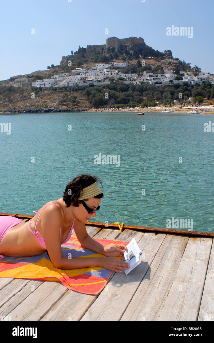 Eine Frau liest auf dem Dock von Lindos bay Insel Rhodos Griechenland Stockfoto