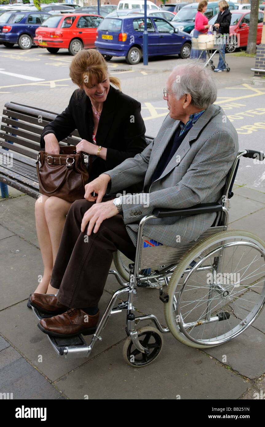 Mann im Rollstuhl im Gespräch mit einer Frau sitzt auf einem hölzernen Sitz Stockfoto
