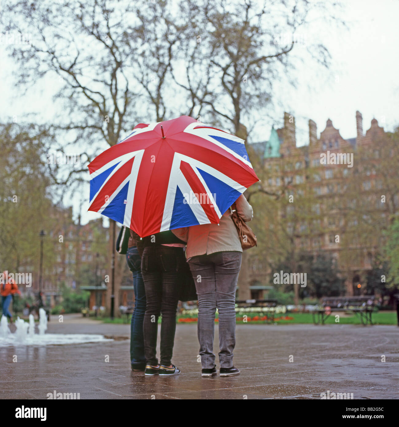 Touristen, die sich vor dem Regen unter einem Schirm der Union Jack Flagge in Russell Square, Bloomsbury London England Großbritannien schützen. KATHY DEWITT Stockfoto