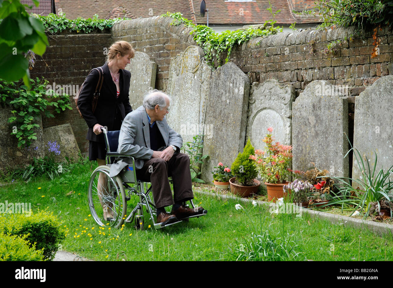Älterer Mann im Rollstuhl geschoben um einen Friedhof mit seinen weiblichen Betreuungsperson Stockfoto