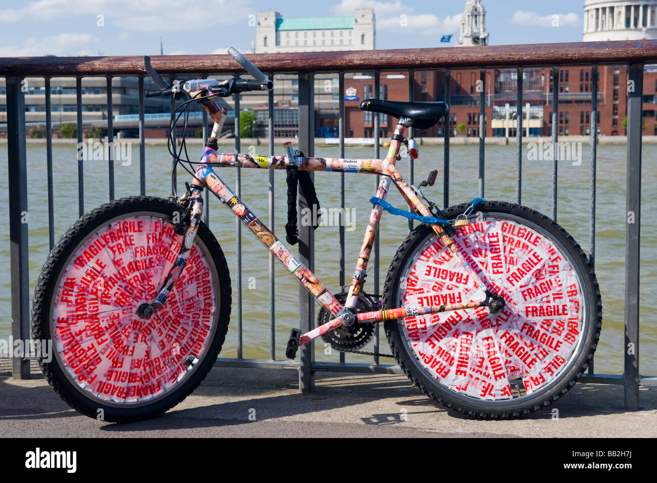 Londoner Southbank, Damm, gut gebrauchtes Fahrrad oder Bike mit einem Vorhängeschloss&angekettet an Zaun oder Geländer durch Wasser der Themse fragile tape Aufkleber Stockfoto