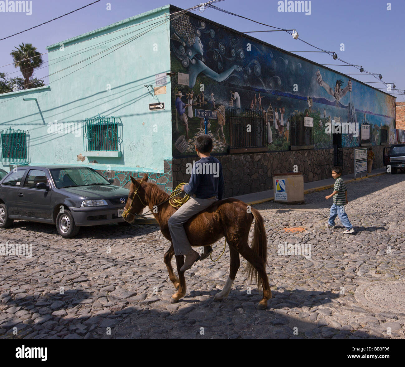 Mexiko, Ajijic. Zwei Kinder, auf Esel, auf einer gepflasterten Straße. Stockfoto