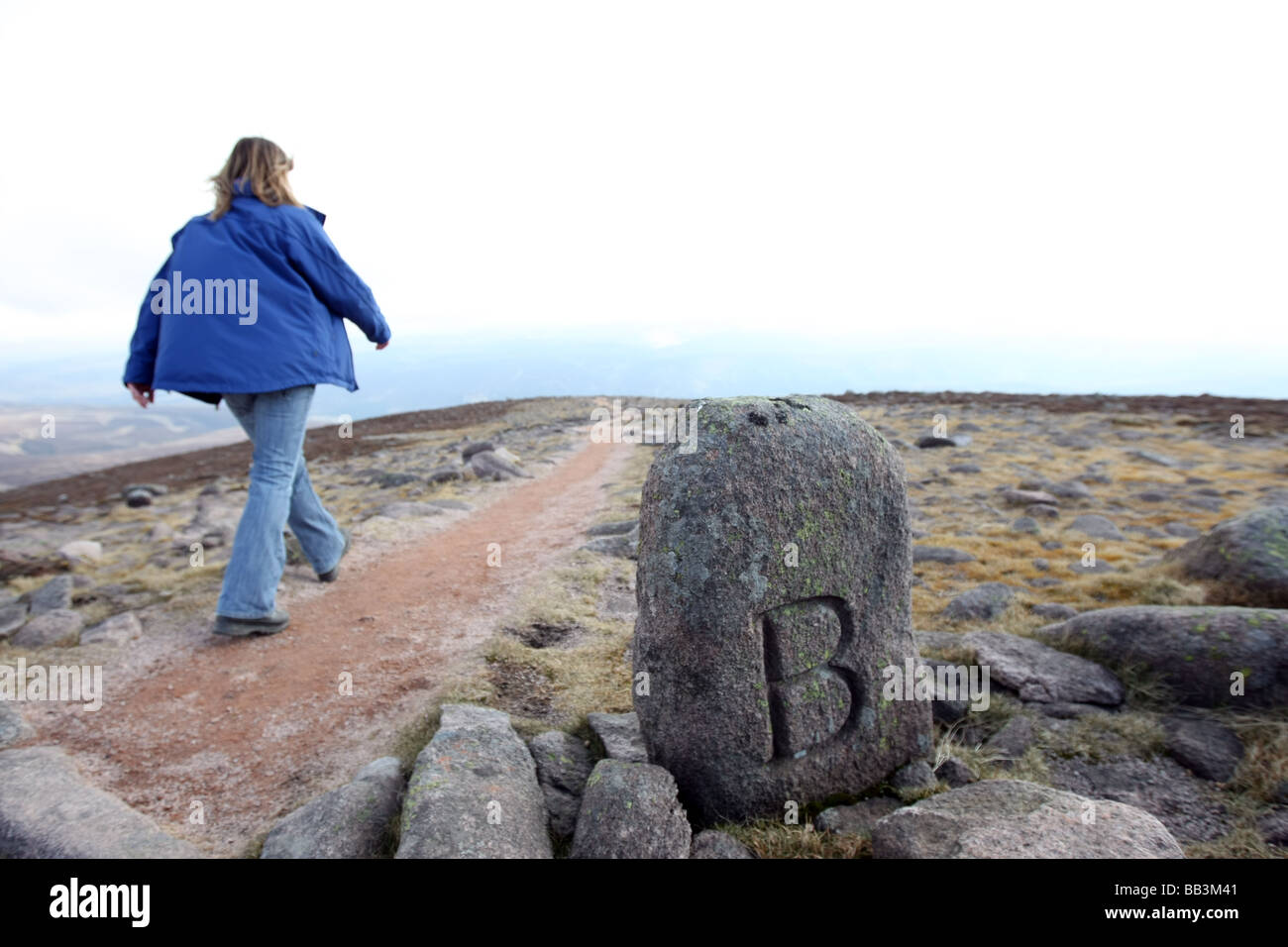 Walker den Weg vom Gipfel des Mount Keen in Glen Esk absteigend, übergibt Angus, Schottland, UK, einen alten Grenzstein Stockfoto