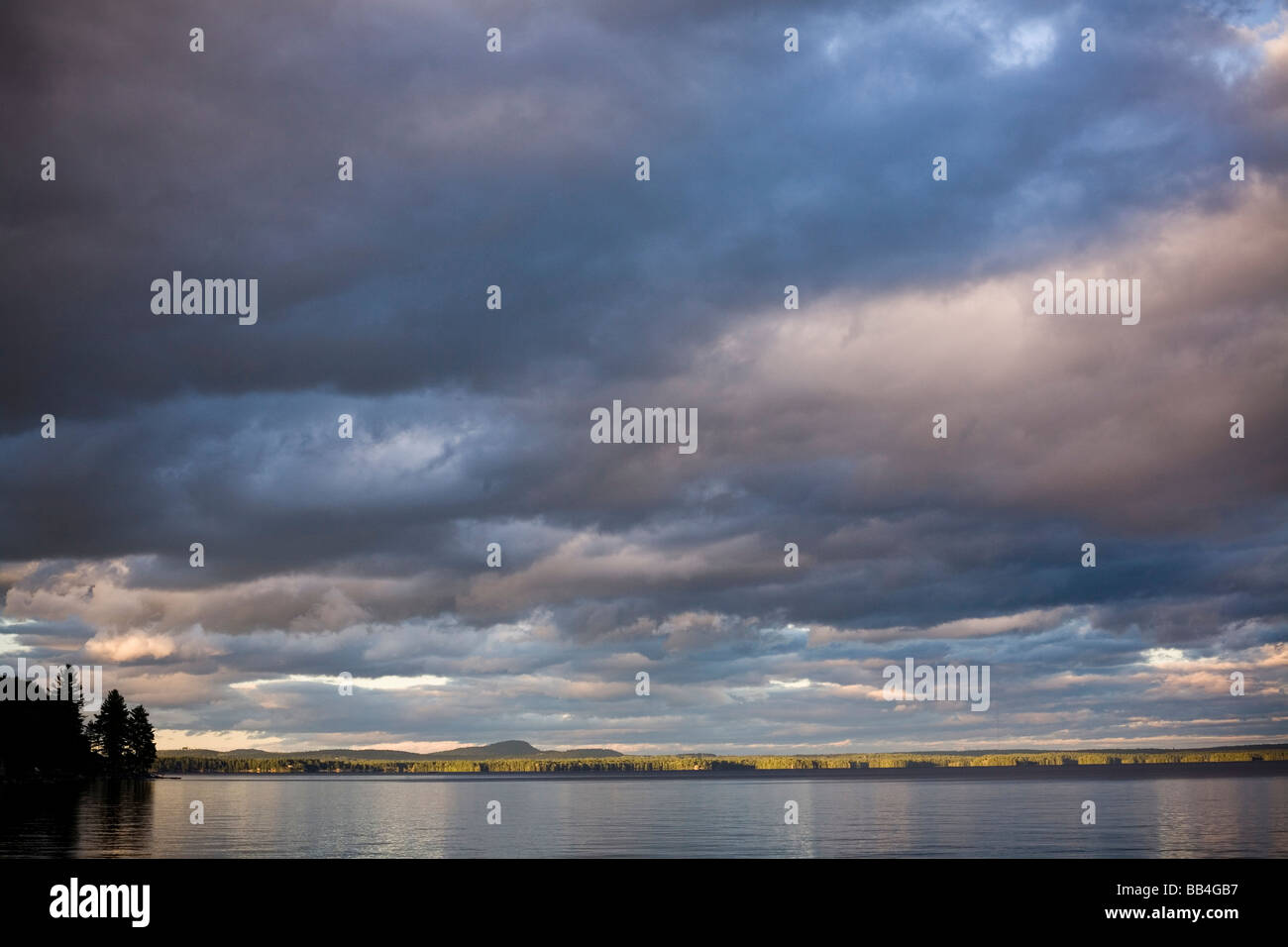 Dramatische, blaue Wolken bilden eine dicke Decke über dem ruhigen Wasser der Sebago See. Stockfoto