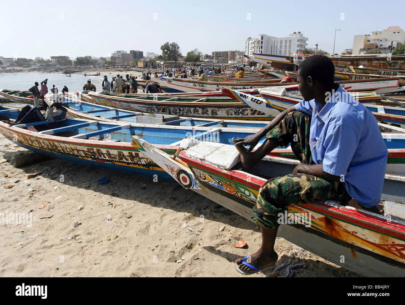 Mann sitzt in einem bunt bemalten Fischerboot am Strand Fisch Markt in Dakar, Senegal Stockfoto