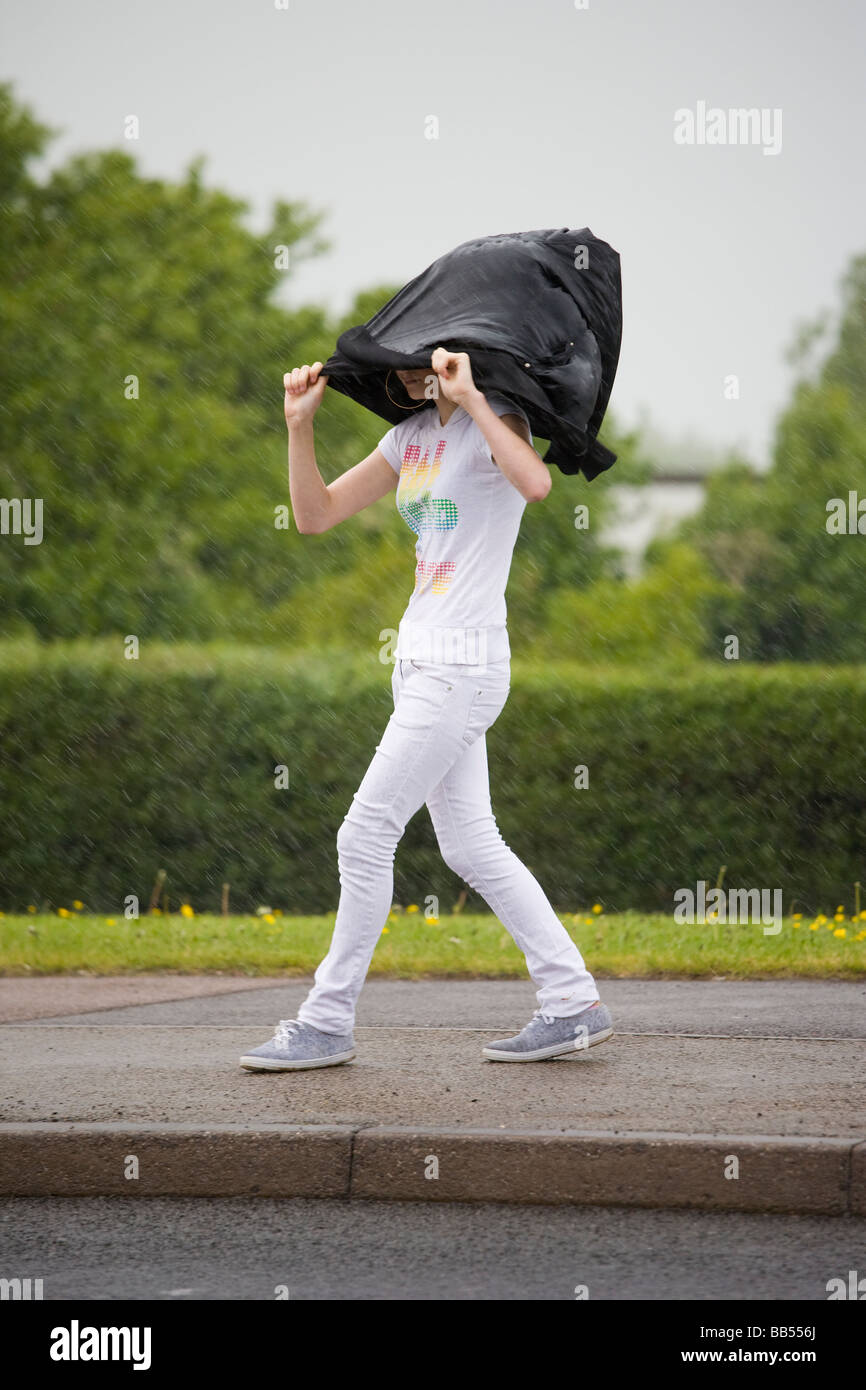 Mädchen Schutz vor Regen durch ihren Mantel über ihrem Kopf Whist Fuß eine Straße halten Stockfoto