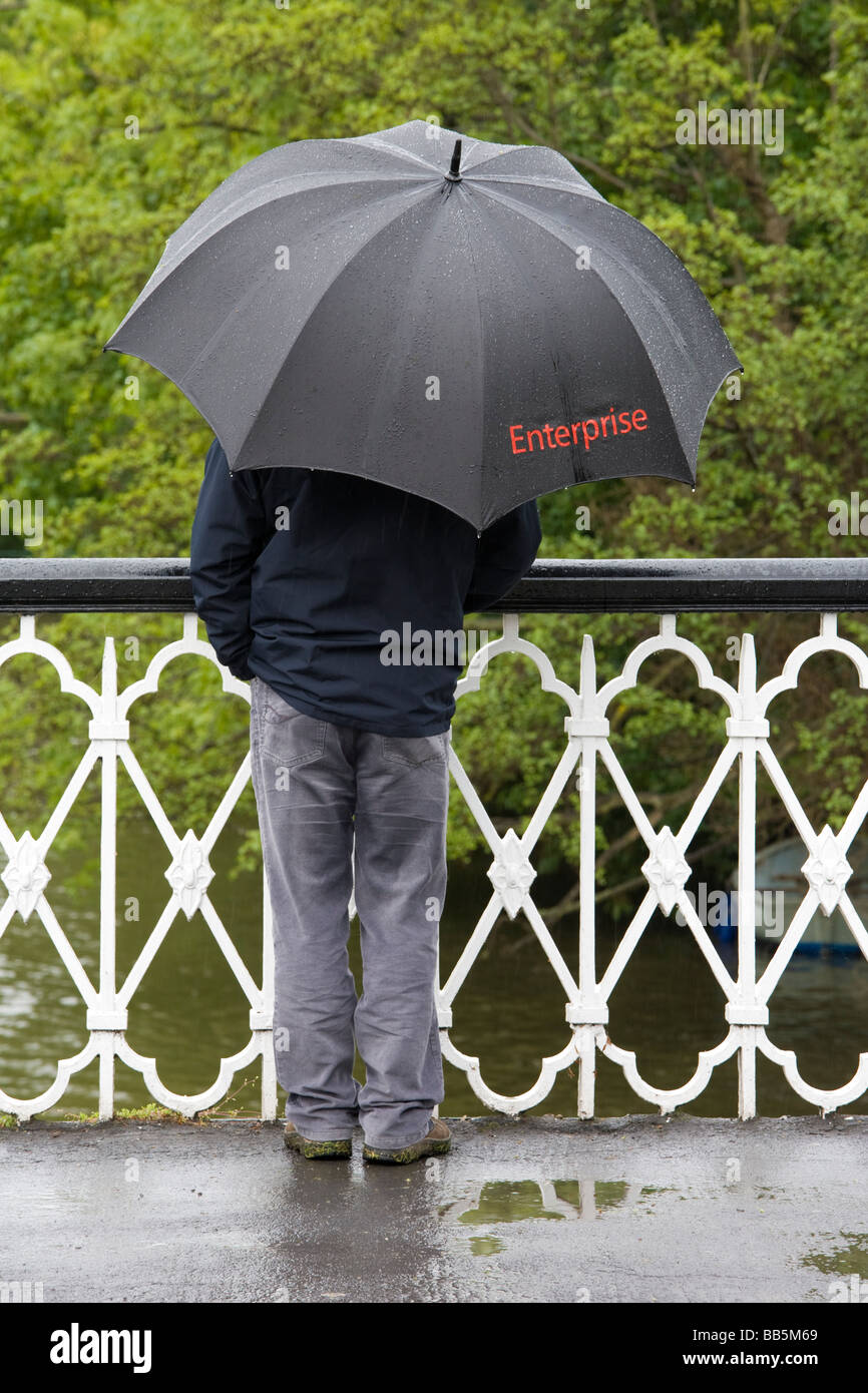 Mann auf der Brücke im Regen stehend mit schwarzen Regenschirm gekennzeichnet Enterprise Stockfoto