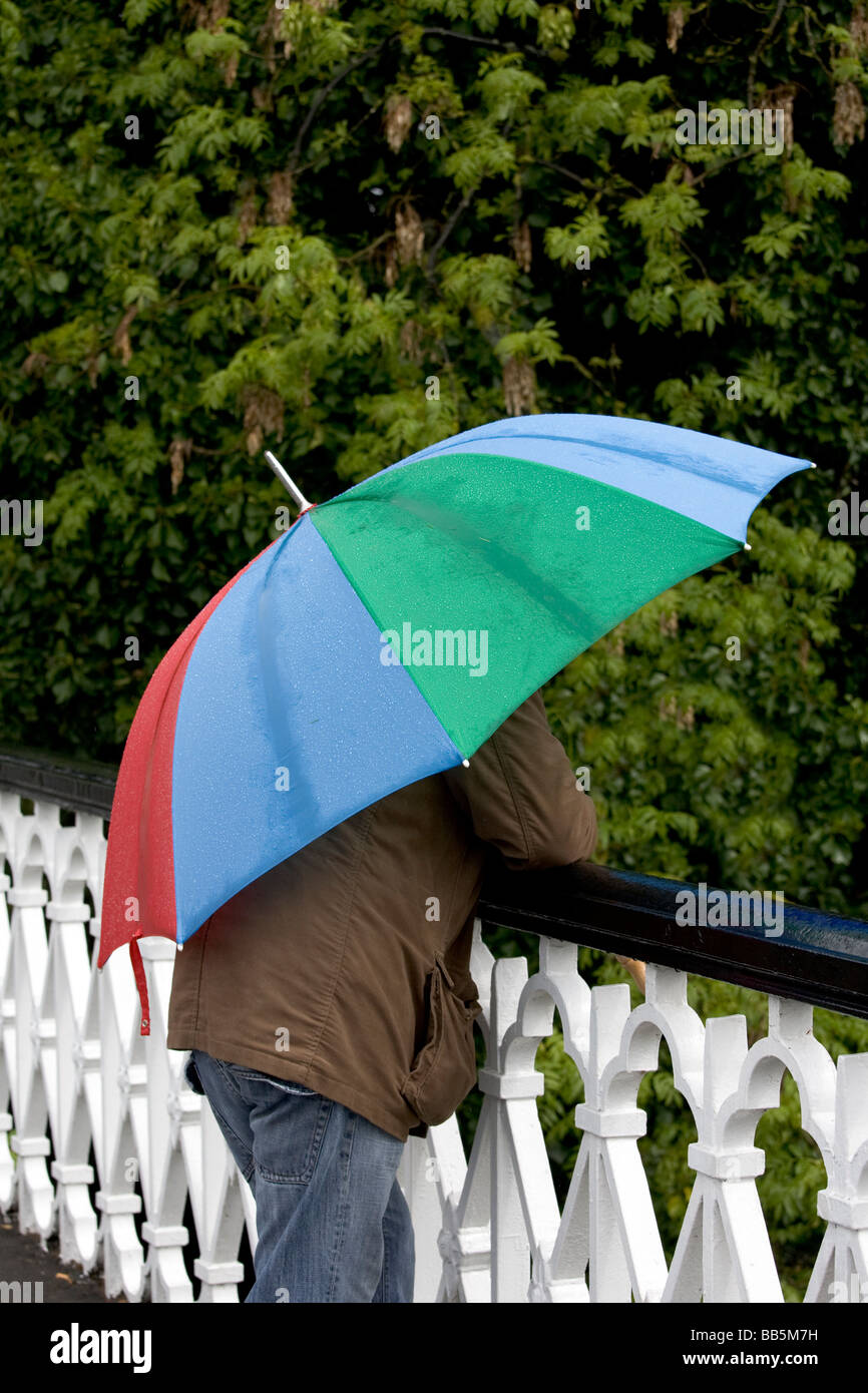 Mann auf der Brücke im Regen mit bunten Regenschirm Stockfoto