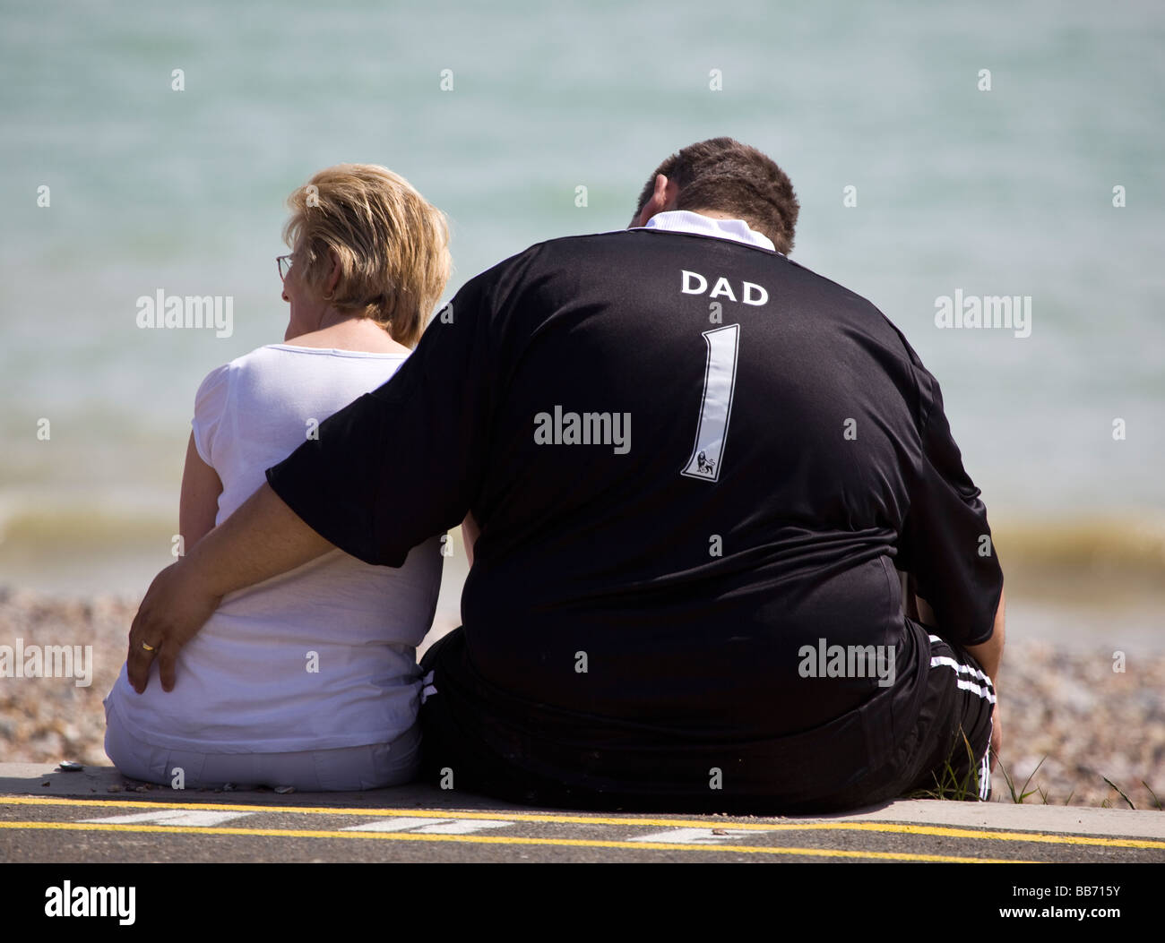 Übergewichtiger Mann mit Nummer eins-Fußballtrikot sitzen am Strand Stockfoto