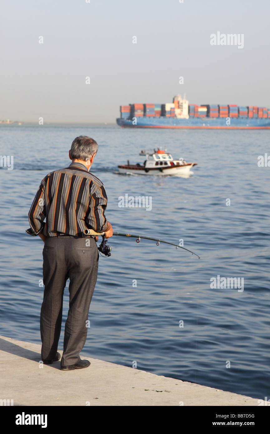 Istanbul Türkei Mann Angeln am Meer in Kumkapi mit großen Containerschiff Schiff hinter den Bosporus verlassen Stockfoto