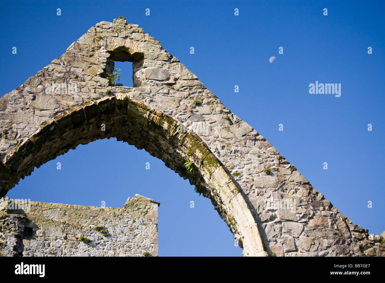 Mondaufgang und Ruinen. Ein gotischer Bogen eines zerstörten Fensters des alten Klosters gleicht der halbe Mond in den strahlend blauen Himmel. Stockfoto