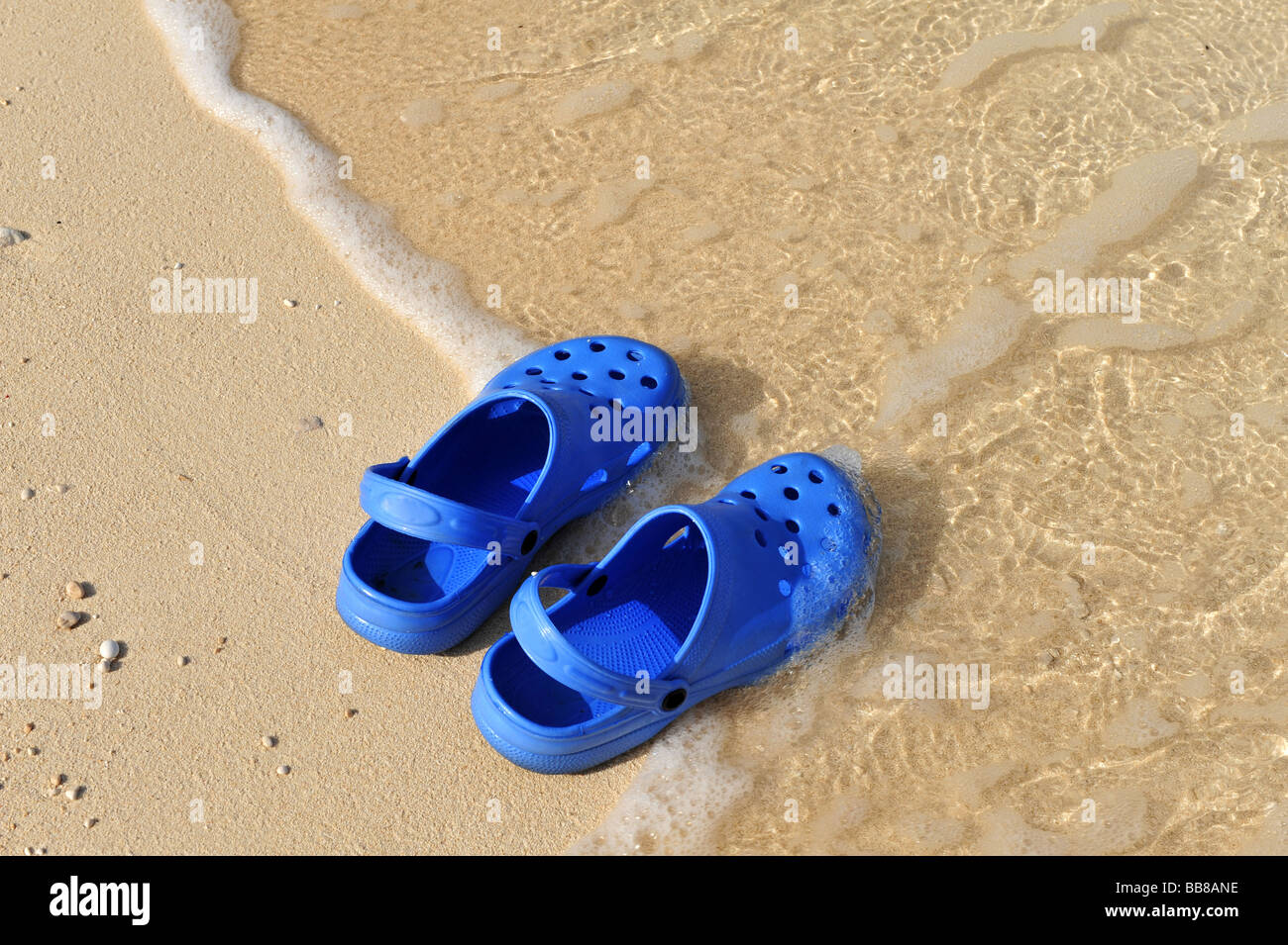 Paar blauer Strand Schuhe oder Krokodile am Rand des Meeres mit einer kleinen Welle und sand Stockfoto