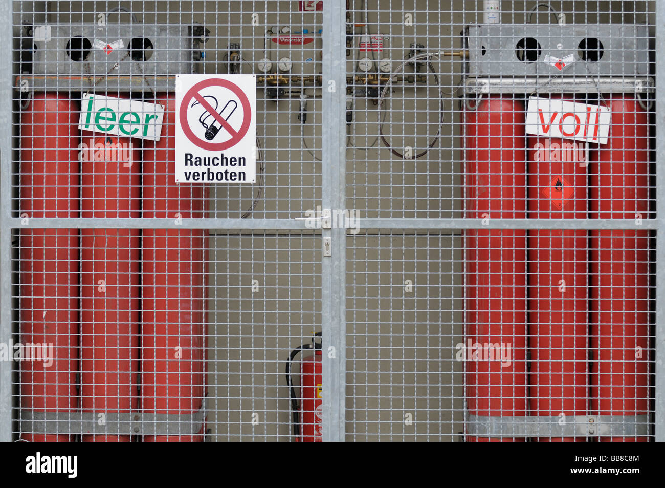 Wasserstofftankstelle nachfüllen, Draht leeren und vollen roten Gasflaschen hinter ein schützendes Netz, Armaturen und Messgeräte, Verbotszeichen Stockfoto