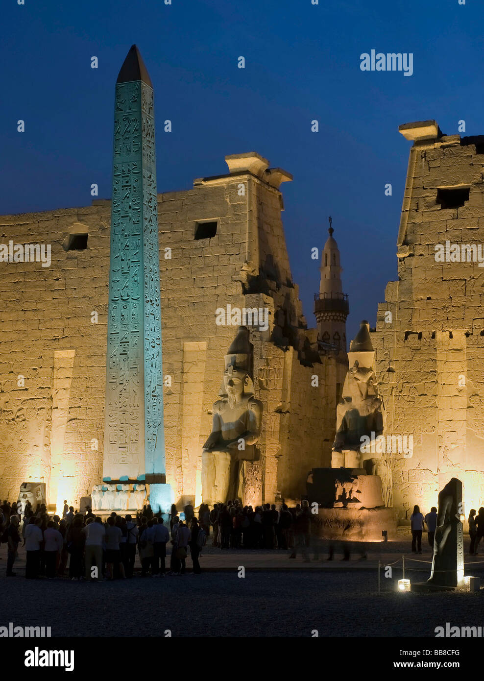 Pylon mit Figuren und Obelisk Ramses II beleuchtet am Abend vor einem Minarett, Luxor-Tempel, Luxor, Ägypten, Af Stockfoto