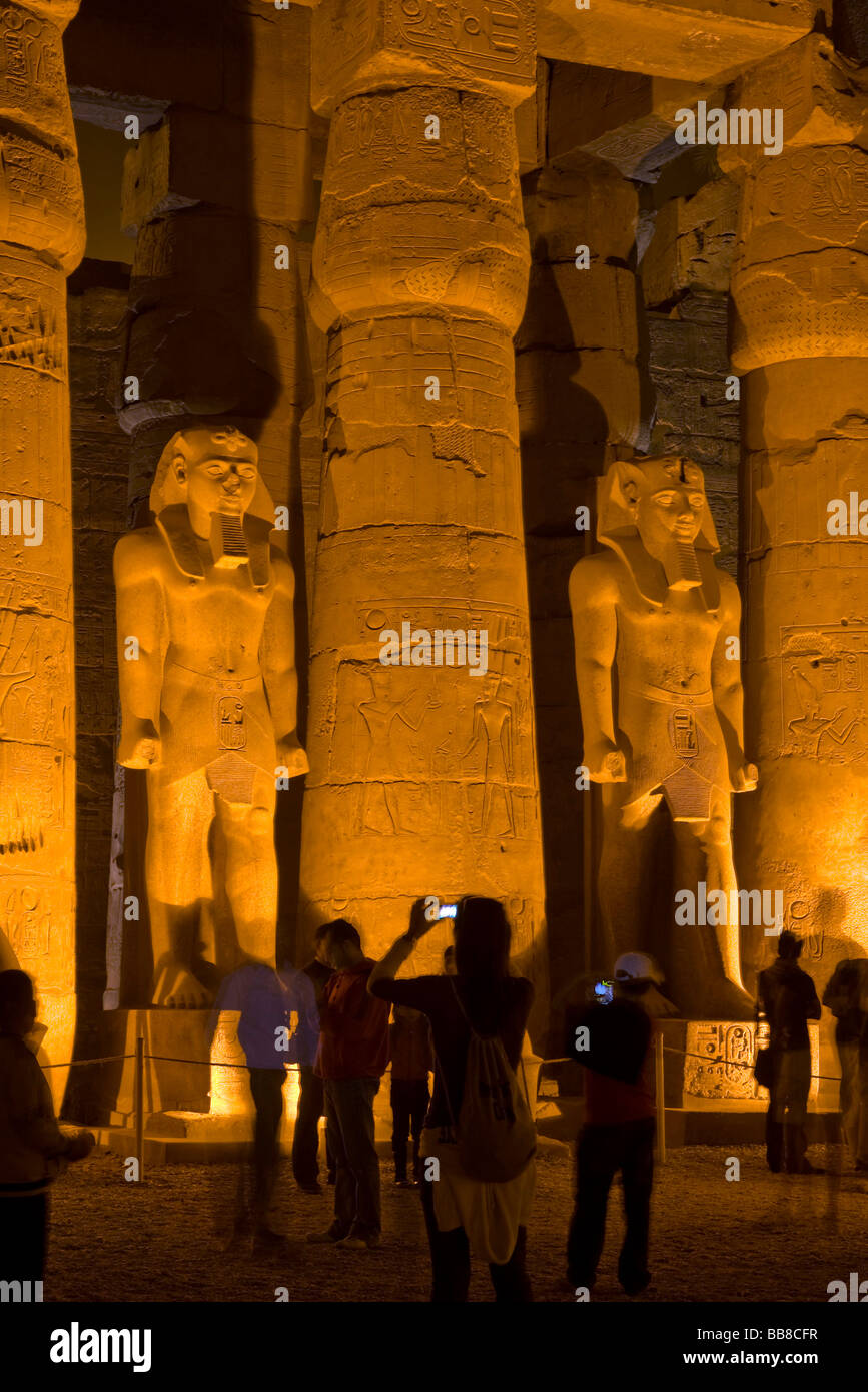 Zwei beleuchtete Statuen von Ramses II, Touristen fotografieren, ersten Innenhof, Luxor-Tempel bei Nacht, Luxor, Ägypten Stockfoto