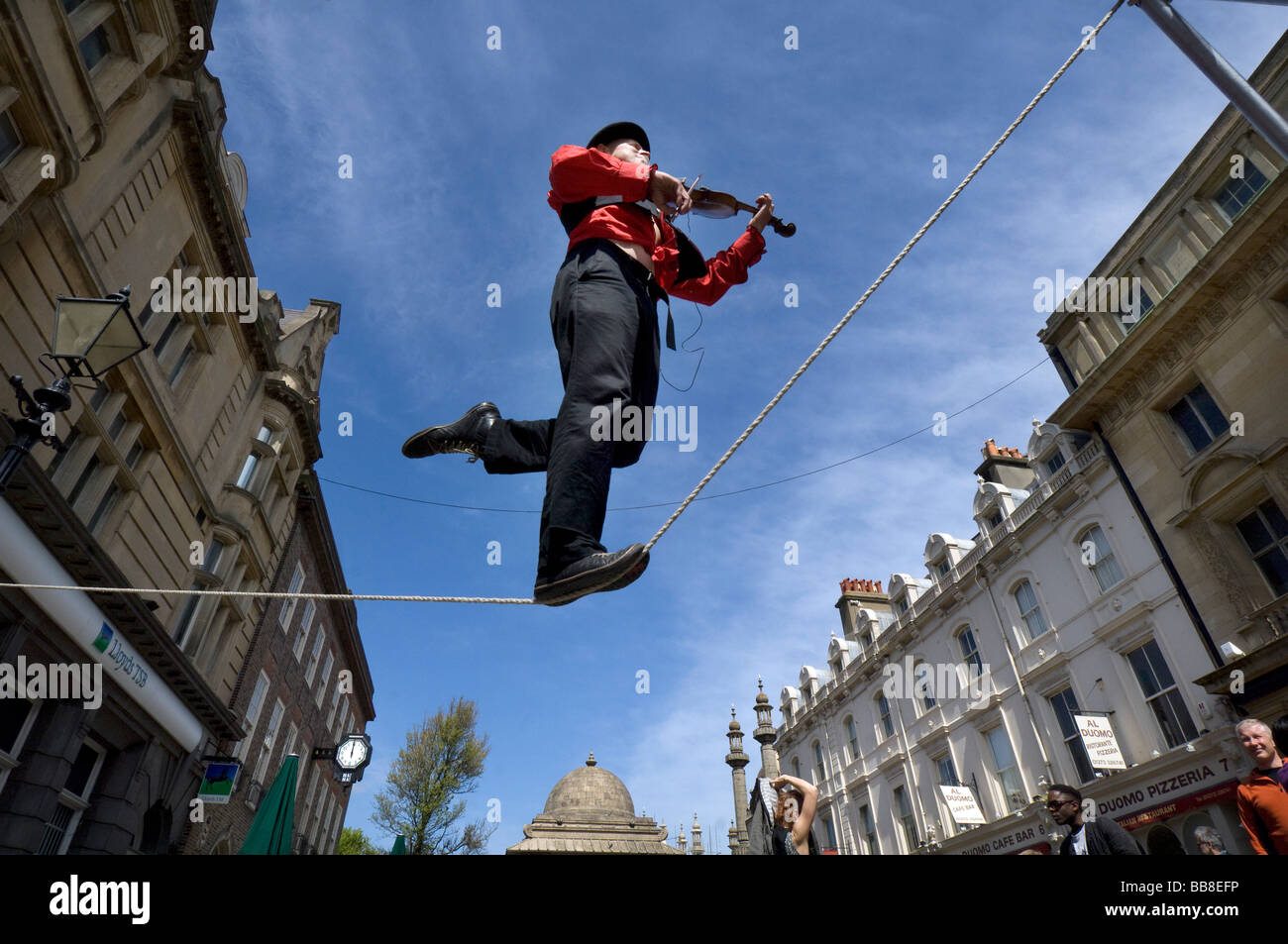 A Street Theatre Straßenmusiker spielt auf einer Violine beim Balancieren auf einem Drahtseil in Brighton Festival Stockfoto