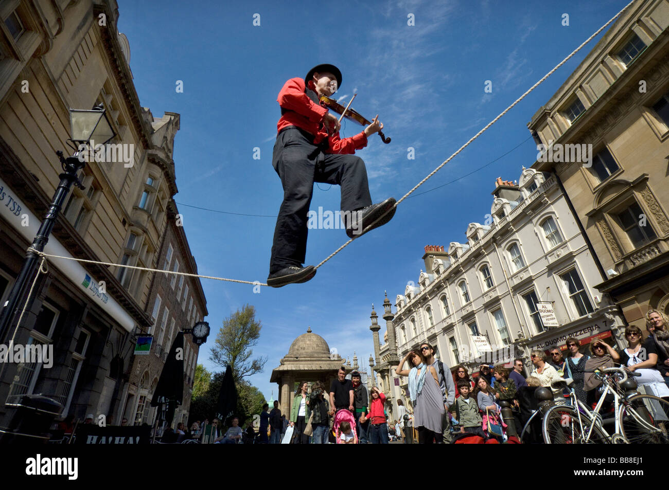 A Street Theatre Straßenmusiker spielt auf einer Violine beim Balancieren auf einem Drahtseil in Brighton Festival Stockfoto