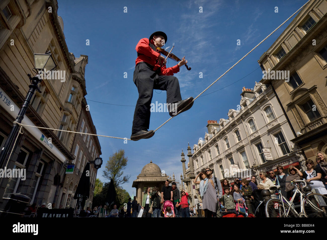 A Street Theatre Straßenmusiker spielt auf einer Violine beim Balancieren auf einem Drahtseil in Brighton Festival Stockfoto