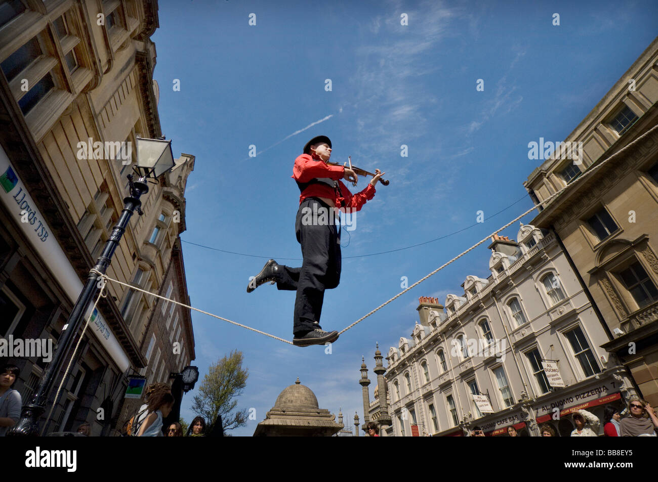 A Street Theatre Straßenmusiker spielt auf einer Violine beim Balancieren auf einem Drahtseil in Brighton Festival Stockfoto