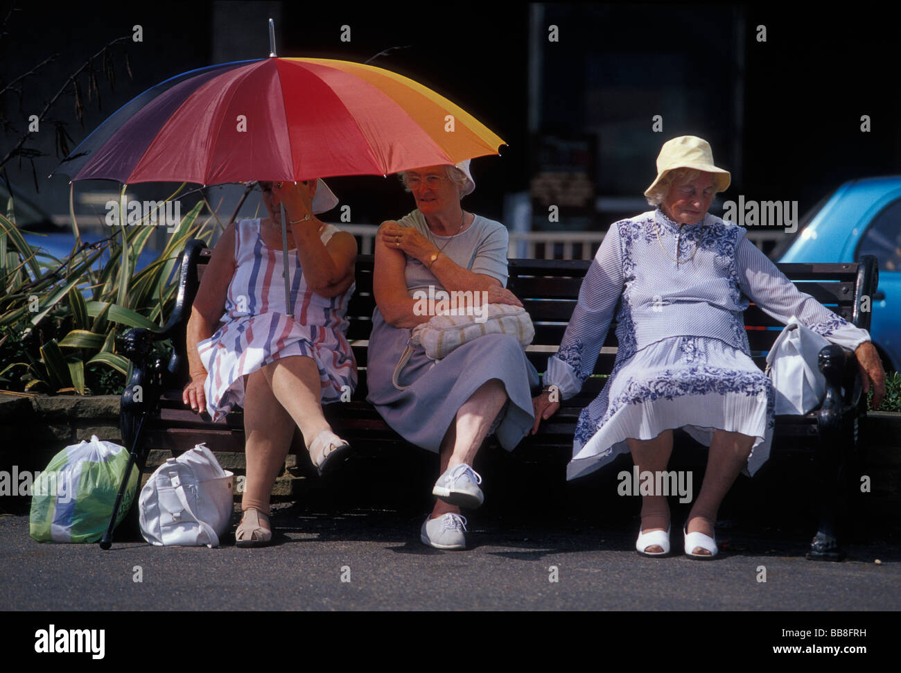 Drei Damen sitzen auf einer Bank im Schatten von der heißen Sommersonne. Worthing. West Sussex Südengland GB. UK Stockfoto