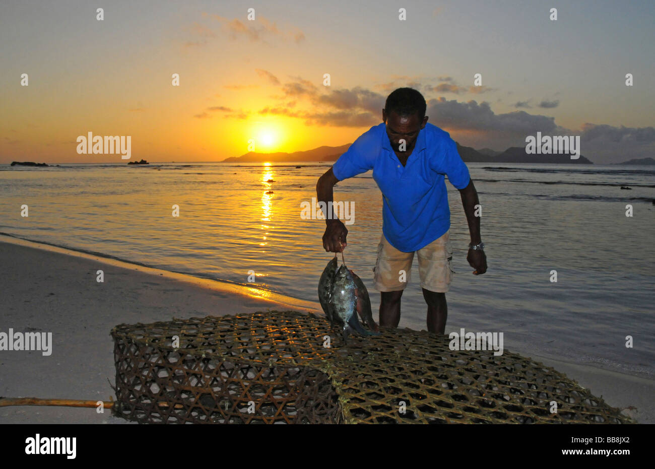Angler mit Fisch vor einem Sonnenuntergang, Anse Severe, La Digue ...