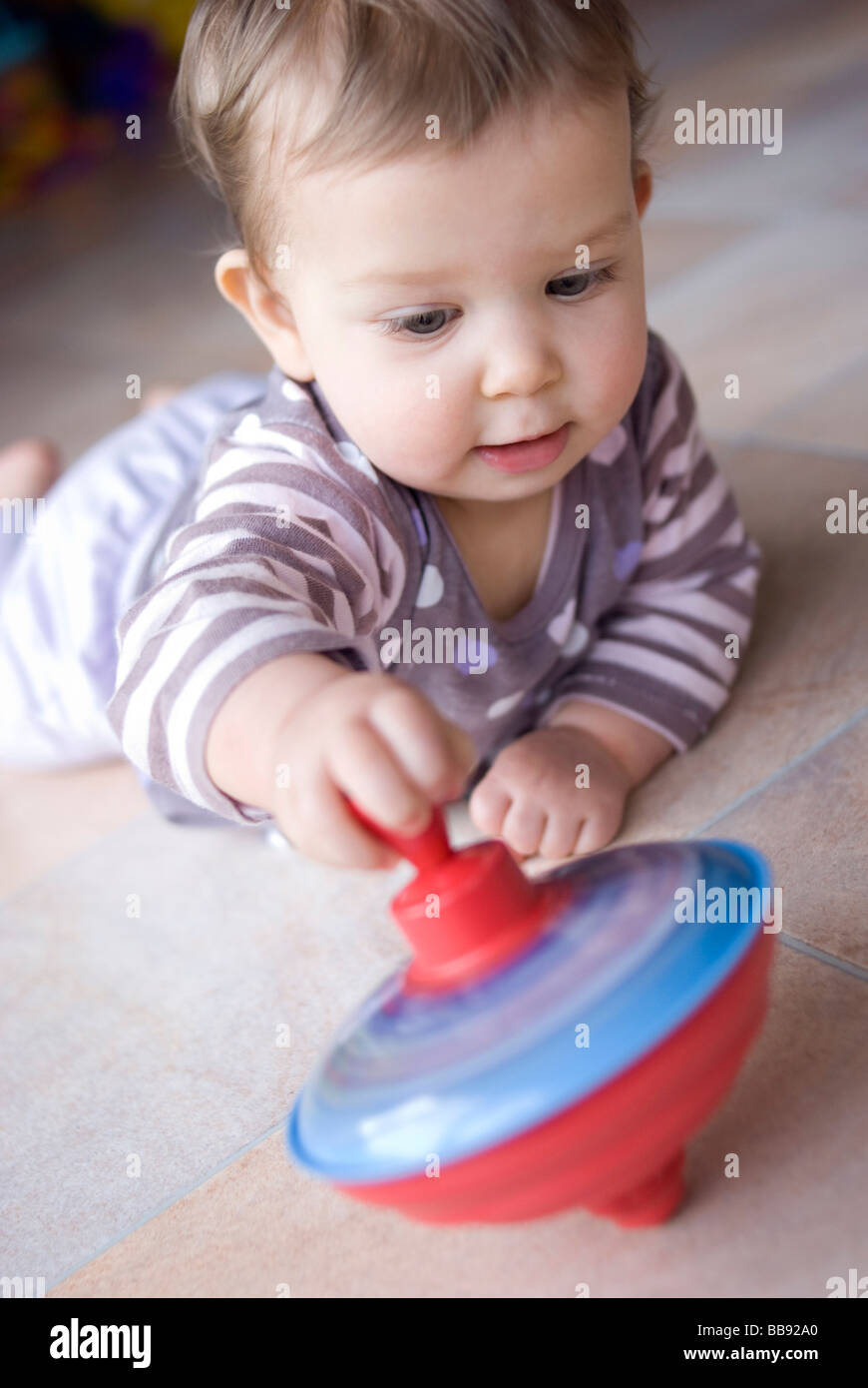 9 Monate altes Baby mit einem traditionellen Spinning Top Spielzeug spielen Stockfoto