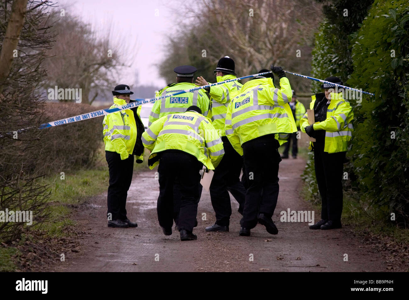 Polizei in gelb fluoreszierenden Jacken überqueren eine Polizeiabsperrung Band auf dem Weg zur Spurensuche nach der Entdeckung eines Körpers Stockfoto