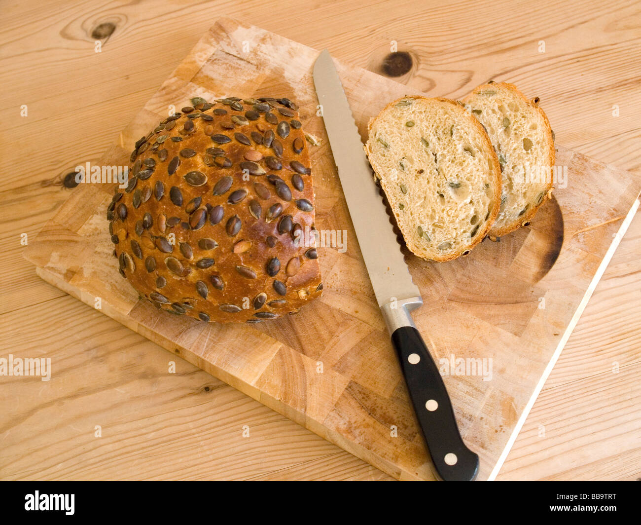 Ein neu geschnittenes Brot aus Stein gebackenes Kürbiskern-Brot mit einem Brotmesser auf einem Holzbrett Stockfoto