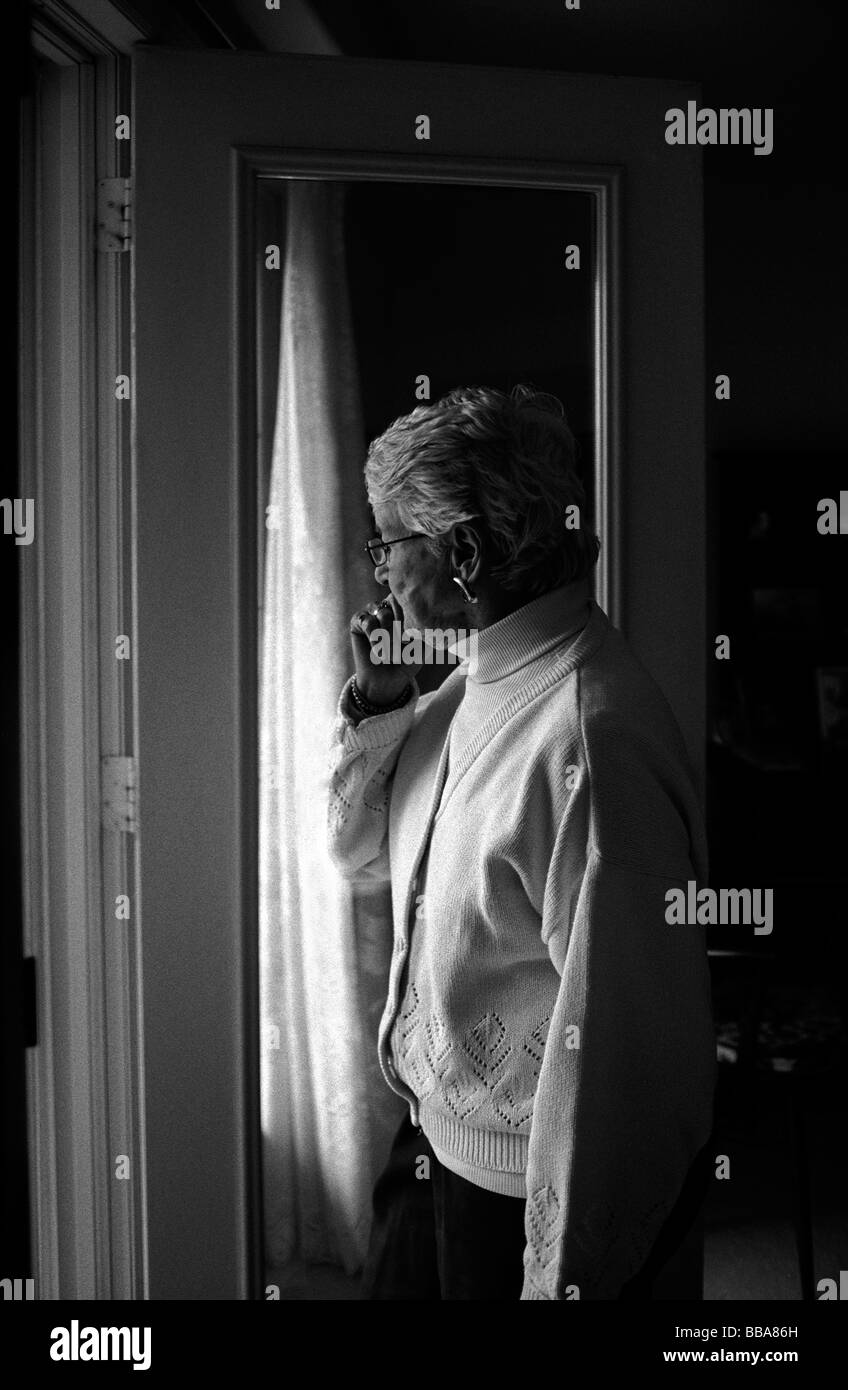 Ältere Frau schaut aus Fenster Vorhang. Stockfoto