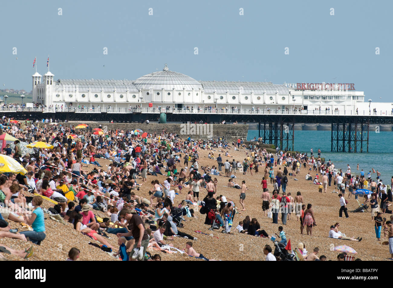 Massen von Urlaubern am Strand von Brighton mit dem Pier im Hintergrund. Stockfoto