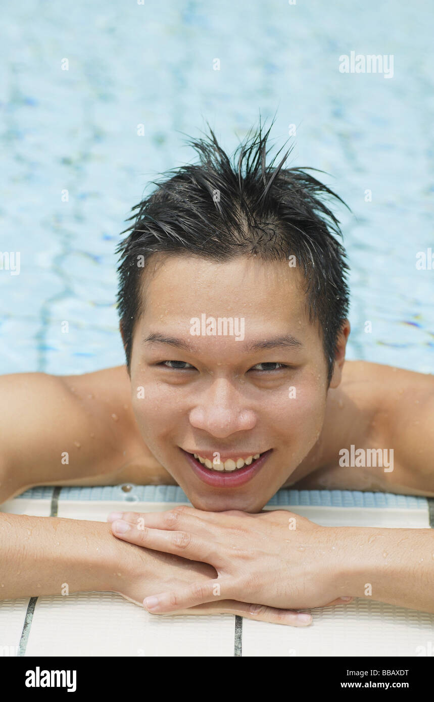 Junger Mann am Rand des Schwimmbads lächelnd in die Kamera Stockfoto