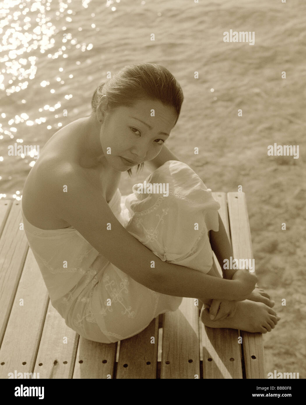 Frau in weißem Kleid sitzt auf Dock, Wasser im Hintergrund, Porträt Stockfoto