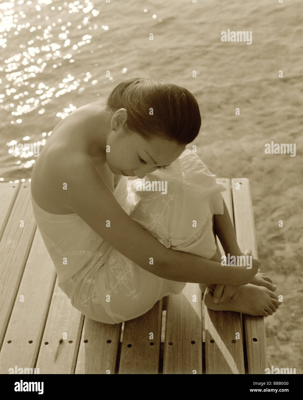 Frau in weißem Kleid sitzt auf der Anklagebank, Wasser im Hintergrund Stockfoto