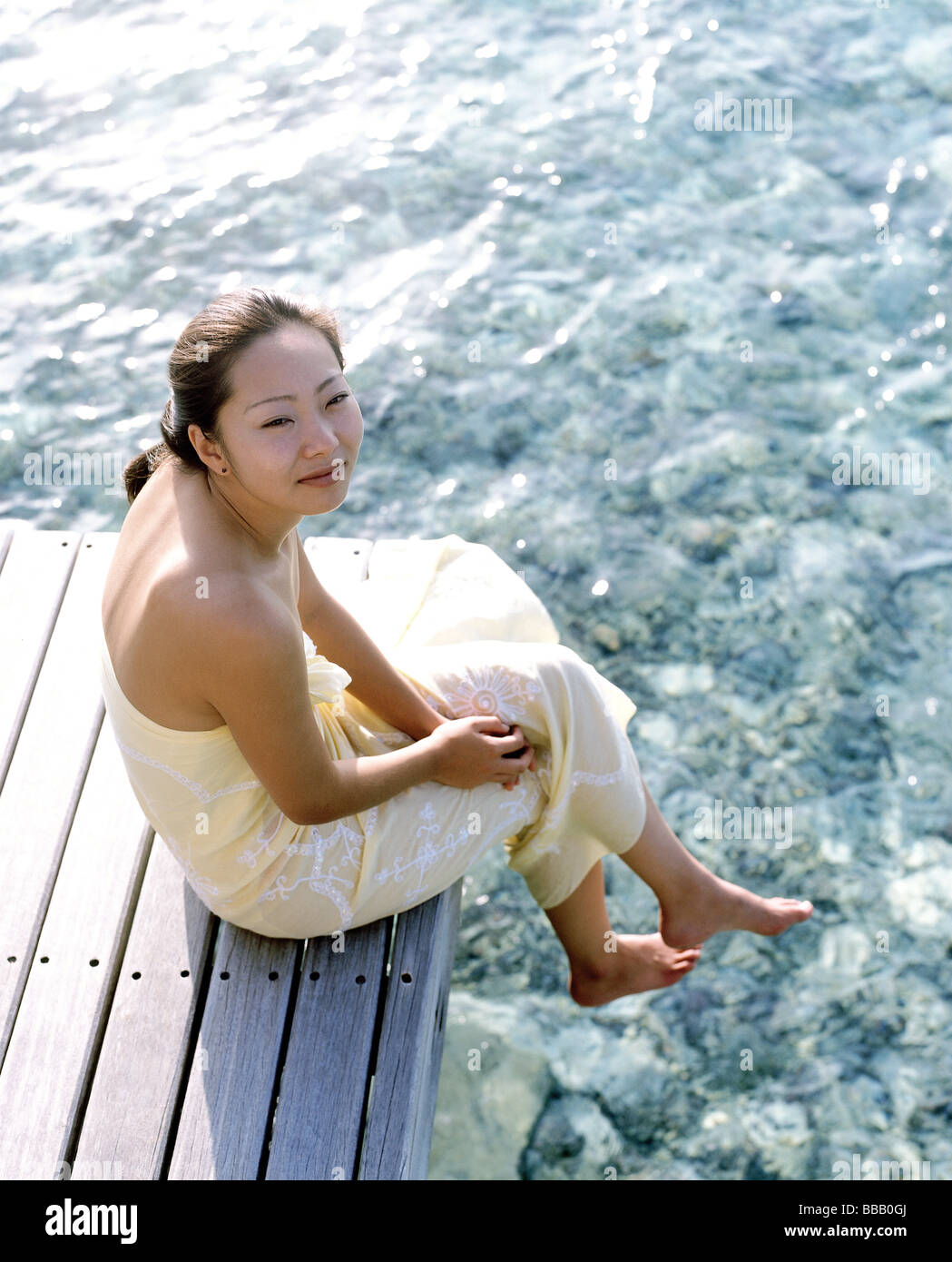 Frau im gelben Kleid sitzt auf dock, Wasser im Hintergrund, Portrait, erhöhter Lage Stockfoto