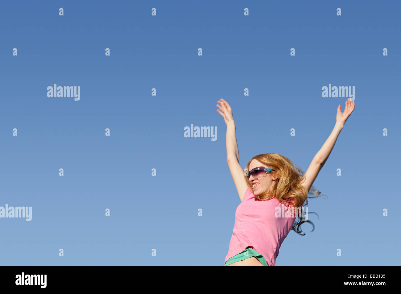 Frau mit vor einem blauen Himmel erhobenen Armen Stockfoto