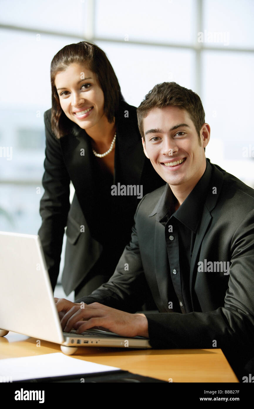Führungskräfte in schwarz gekleidet, sitzt neben Laptop, Blick in die Kamera, Lächeln Stockfoto
