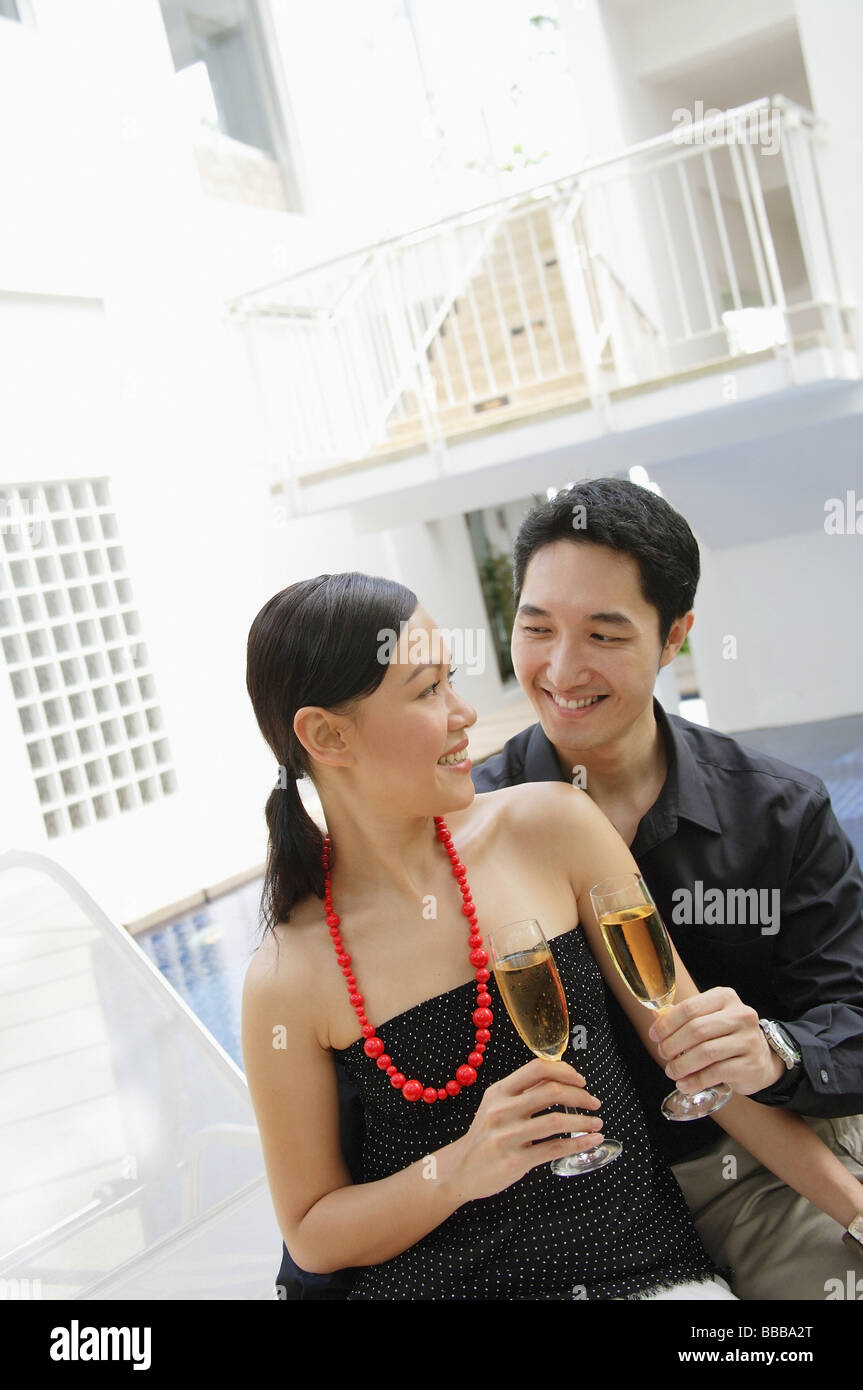 Paar sitzt am Pool, einander betrachtend, hält Champagner Gläser Stockfoto