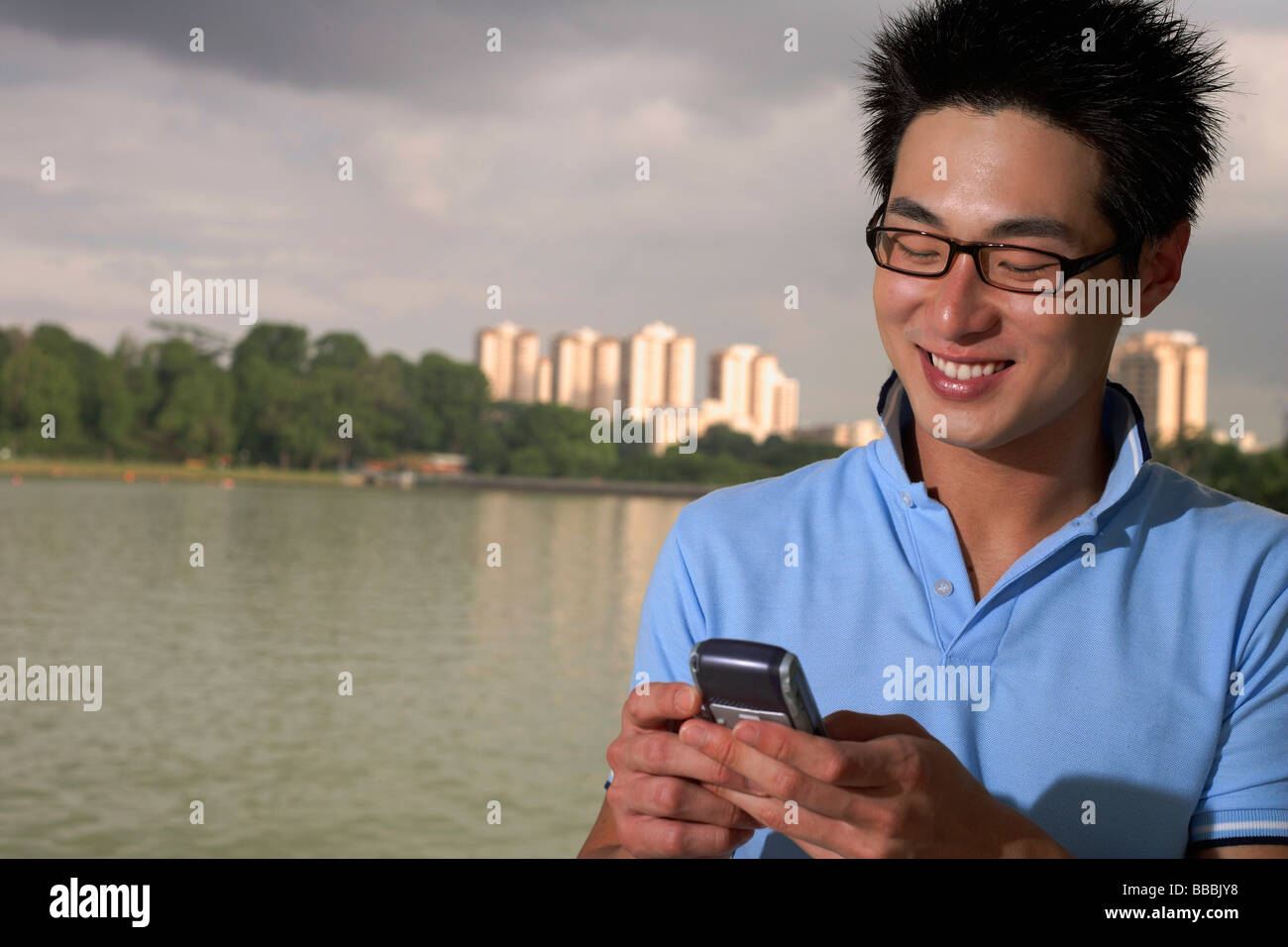 Mann am Handy, Körper von Wasser und Gebäuden im Hintergrund Stockfoto