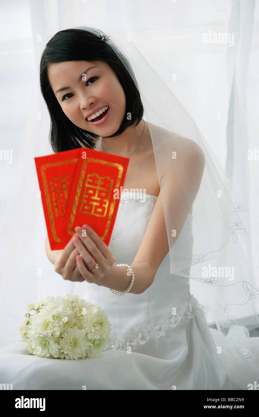 Eine Braut in die Kamera lächelt und hält Sie zwei rote Umschläge Stockfoto